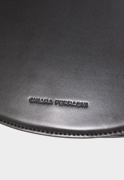 Sort lædertilbehør med en glat overflade, der har et præget "CHIARA FERRAGNI" logo forneden. Rund form med rene kanter.