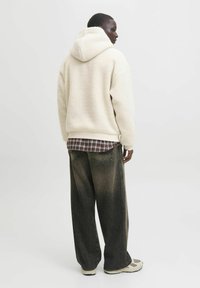 Crème fleece hoodie met een zachte textuur, gedragen over een geruit shirt. Gecombineerd met donkere, wijde jeans en lichte sneakers.