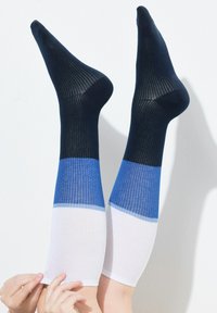 Calze al ginocchio a coste con design a blocchi di colore: sezioni di blu scuro, blu e bianco con una texture liscia e una forma aderente.