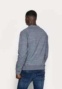 Grijze sweatshirt van een geaccentueerde, gemêleerde stof, met een ronde halslijn en raglanmouwen, gecombineerd met donkerblauwe jeans en zichtbare achterzijde kenmerken.