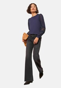 Meresinine pullover tekstuurse, läbipaistva pitsist varrukatega; mustad laia säärega teksad; pruun käekott; mustad terava ninaga kontsakingad; vabaaja rõivastus.