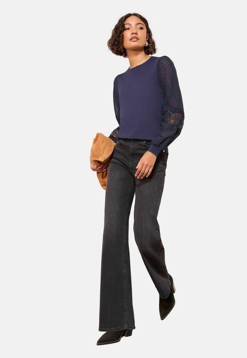 Meresinine pullover tekstuurse, läbipaistva pitsist varrukatega; mustad laia säärega teksad; pruun käekott; mustad terava ninaga kontsakingad; vabaaja rõivastus.