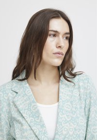 Světle modrý blazer s složitým vzorem srdcí, s klopou a měkkou texturou, nošený přes bílý žebrovaný top.
