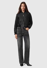 Chaqueta bomber de cuero negro con diseños en relieve, combinada con jeans negros de tiro alto y desgastados, y tacones negros puntiagudos.