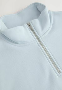Lichtblauwe zip-hals sweatshirt van zacht materiaal, met een hoge kraag en een zilveren rits aan de voorkant, met minimale stikseldetails.