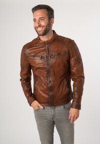Bruine leren motorjack met een mandarin kraag, ritsopening aan de voorkant en zakken, en gestikte details op de schouders. Gladde textuur.