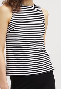 Top sin mangas a rayas en blanco y negro con un cuello alto, hecho de una tela suave, con rayas uniformes y un corte relajado.