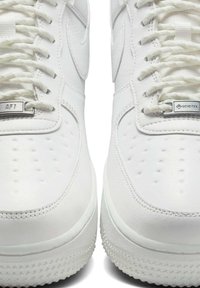 White leather sneakers with a textured surface, featuring perforations, white laces, and silver hardware labeled "AF1" and "GORE-TEX."