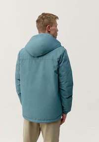 Zelena pufasta jakna z velikim kapuco, brezšivnim dizajnom in elastičnimi manšetami. Material se zdi gladek in trpežen, s nekoliko sijočim zaključkom.