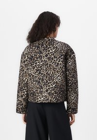 Veste en imprimé léopard avec une texture matelassée, dotée d'un col rond, d'accents noirs et d'un design court. Un pantalon large noir est visible.