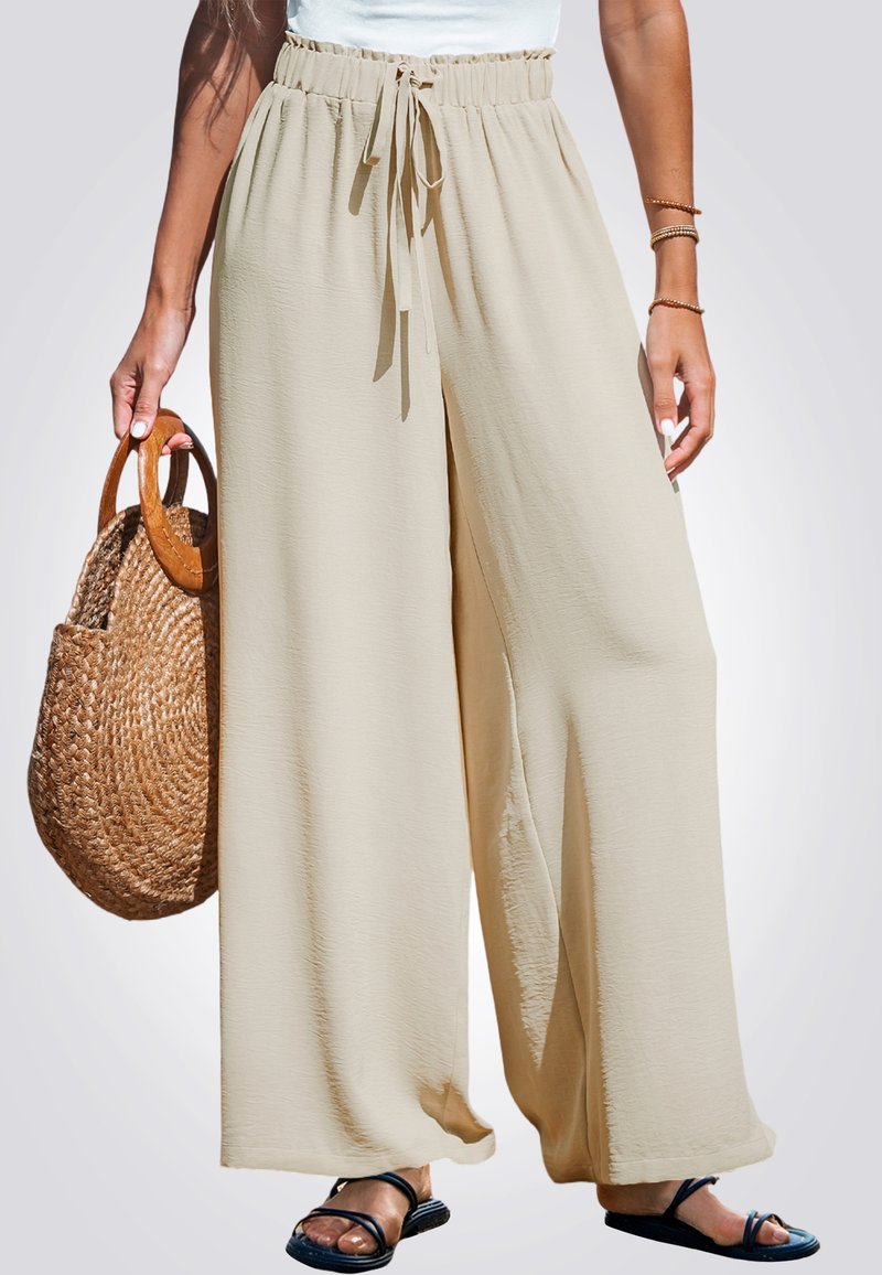 Pantalones de pierna ancha beiges con una alta cintura elástica y un cordón atado. Tejido liviano con una textura fluida; combinados con un bolso de mimbre.