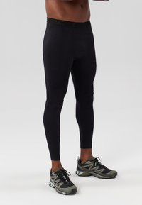 Juodi tamprės su lygiu paviršiumi ir prigludusia forma, su logotipo dekoruota juosmeniu. Dėvimos su pilkais ir juodais sportiniais batais.