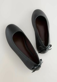 Juodi odiniai baleto bateliai su apvaliu priekiu ir maža atlasine kaspinėlio detalė ant kulno. Lygus paviršius ir minimalistinis dizainas.