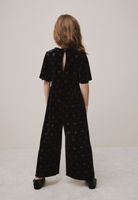 Tuta intera in velluto nero con motivo a cuore texturizzato, maniche corte e dettaglio a goccia sulla schiena, con pantaloni a gamba larga.