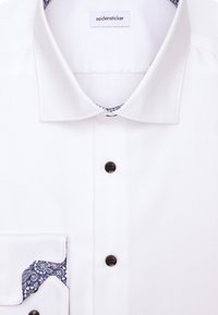 Camicia bianca con bottoni neri, motivo paisley blu a contrasto all'interno del colletto e dei polsini, etichetta del marchio "seidensticker" visibile all'interno del colletto.