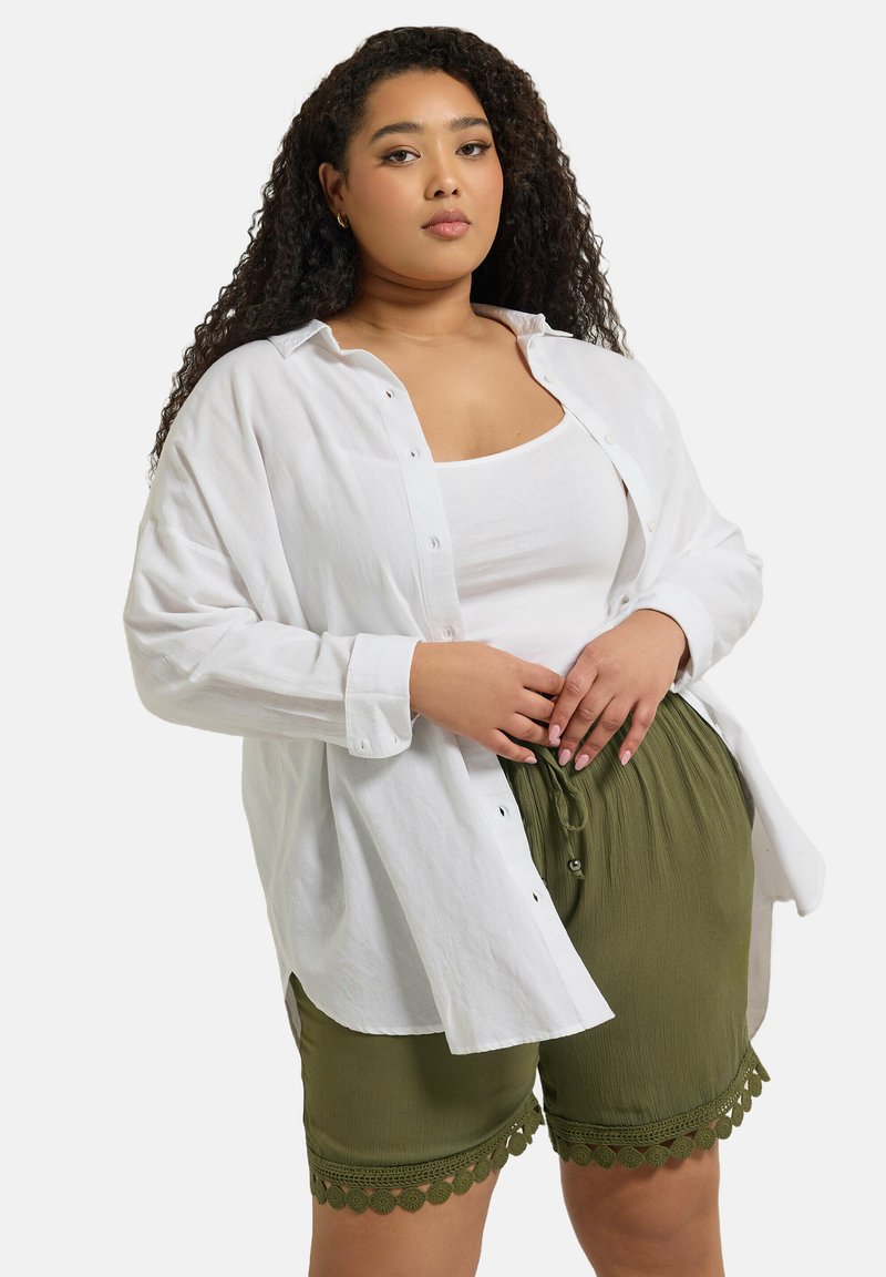 Vit skjorta med knappar över en vit linne, matchad med olivgröna stretchshorts med elastisk midja och scallopdetaljer vid sömmen.