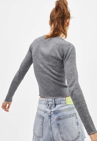 Grå, ribbad långärmad topp med en figurnära silhuett, kombinerad med bleka jeansshorts med en synlig etikett på midjebandet.