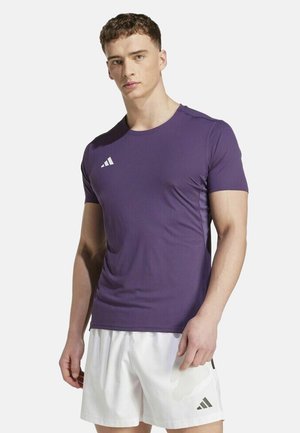 Camiseta deportiva morada de manga corta con cuello redondo, que presenta el logo de tres franjas blancas en el pecho izquierdo. Textura de tela suave.