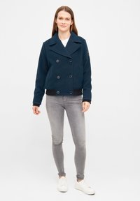 Giacca doppiopetto in misto cotone blu navy con grandi bottoni e design cropped. Presenta una banda nera solida all'orlo.