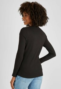 Schwarzes, geripptes Langarmoberteil mit Rundhalsausschnitt und slim fit. Das Design umfasst einen abgerundeten Saum und wird mit hellblauen Jeans kombiniert.