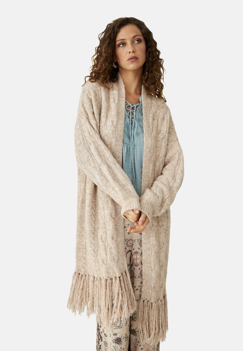 Cárdigan de punto de cable en beige claro, con mangas largas y detalle de flecos en el dobladillo. Textura suave, diseño de apertura en la parte delantera.