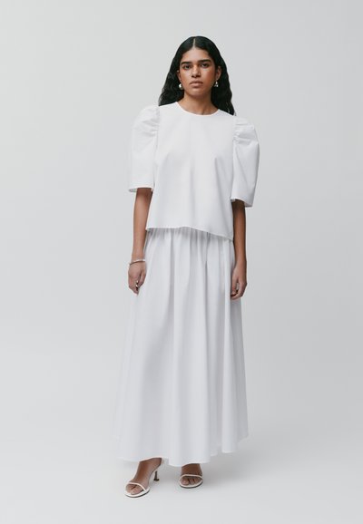 Weißes Zweiteiler-Outfit mit einem kurvenbetonten Top mit Puffärmeln und einem langen, fließenden Rock aus glattem Stoff.