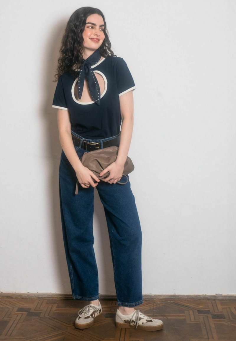 T-shirt navy con taglio e bordo bianco, abbinata a jeans blu a vita alta. Accessoriata con una pochette marrone e scarpe a fantasia.