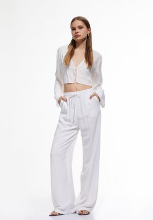 Witte geknipte blouse met een strik aan de voorkant en lange mouwen, gecombineerd met hoge, ruime witte broeken. Glad stoffen textuur.