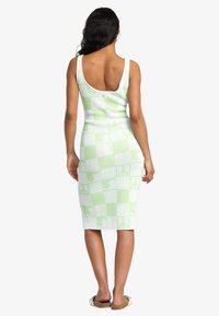 Abito bodycon a scacchi verde e bianco con scollo a barca, realizzato in un tessuto tricot strutturato che si adatta al corpo.