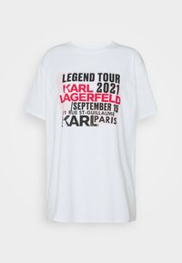Bílý bavlněný tričko s výrazným, vícebarevným textem: "LEGEND TOUR 2021 KARL LAGERFELD," s daty a místem vytištěnými v různých velikostech.
