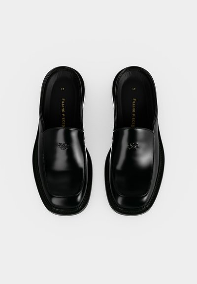 Ζευγάρι μαύρα γυαλιστερά δερμάτινα loafers χωρίς κορδόνια με τετράγωνες μύτες και διακριτικό ανάγλυφο λογότυπο στην κορυφή, εμφανιζόμενα από πάνω σε λευκό φόντο.