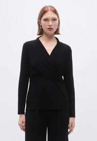 Zwart wikkelshirt met lange mouwen van een gladde, rekbare stof. Heeft een V-hals en plooidetail bij de taille, wat zorgt voor een getailleerde silhouet.