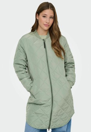 Veste longue matelassée en vert clair, avec une fermeture éclair sur le devant, des poches latérales et des poignets côtelés. Le tissu a une finition lisse et brillante.