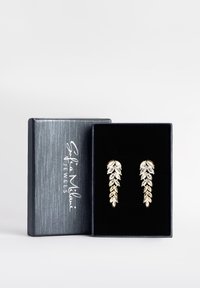 Orecchini a forma di foglia con tonalità dorate e accenti in cristallo trasparente, esposti in una scatola rivestita in velluto nero con un coperchio grigio testurizzato.