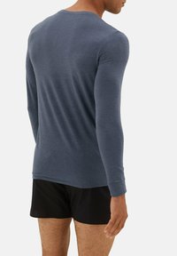 Langærmet grå skjorte lavet af blødt stof, med rund hals og tætsiddende design, kombineret med sorte shorts, set fra bagsiden.