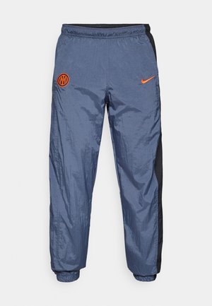 Plave najlon hlače za trčanje s elastičnim pojasom. Imaju crne bočne panele i narančasti Nike logo na lijevoj butini. Glatka, lagana tekstura.