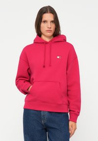 Rosa hettegensere med frontlomme og snorer, med en liten logo. Laget av tykk, myk stoff. Løs passform, uformell stil.