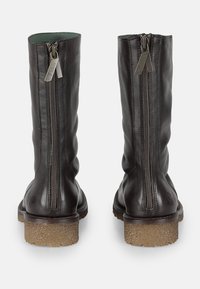 Bottes en cuir marron hautes jusqu'au genou avec une surface texturée, des zips latéraux et une semelle en caoutchouc épaisse. L'intérieur est doublé de vert.