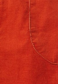 Tecido de veludo cotelê laranja com riscas verticais, apresentando um bolso e costura contrastante ao longo das bordas e costuras.
