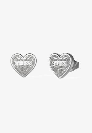 Boucles d'oreilles en argent en forme de cœur, ornées de cristaux et portant le logo "GUESS" en relief, avec une finition lisse et polie.