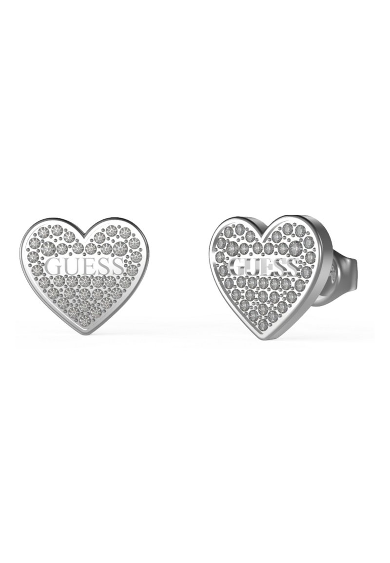 Boucles d'oreilles en argent en forme de cœur, ornées de cristaux et portant le logo "GUESS" en relief, avec une finition lisse et polie.