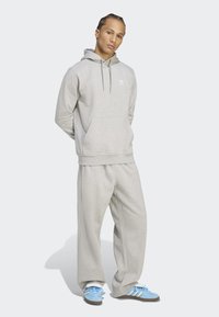Gray hoodie with kangaroo pocket, matching gray joggers, and blue sneakers featuring three stripes. Soft texture and relaxed fit.