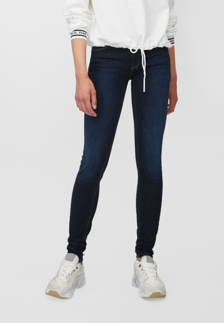 Jeans ajustados de denim azul oscuro, con un diseño ceñido, cintura de tiro medio y detalles de costura sutiles, combinados con zapatillas blancas.
