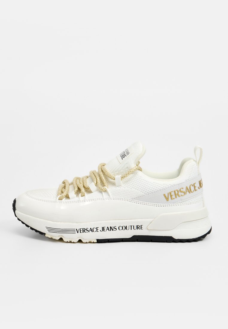 Zapatillas blancas Versace Jeans Couture con cordones de cuerda dorados, parte superior de malla y suela negra con marca, sobre un fondo blanco.