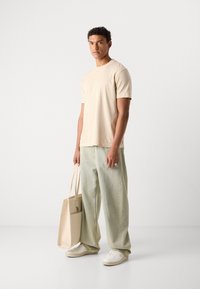 Beige cotton T-shirt, relaxed fit, paired with light-wash baggy jeans, white sneakers, and a beige tote bag. Simple design, minimal accents.