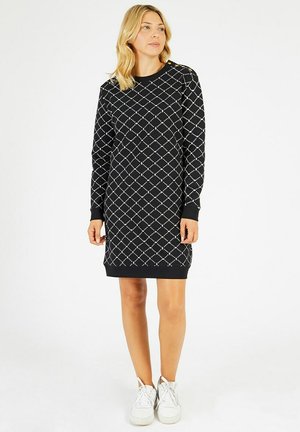 Robe noire en tissu doux, avec un motif en diamant, des manches longues et des poignets côtelés. Associée à des baskets blanches.