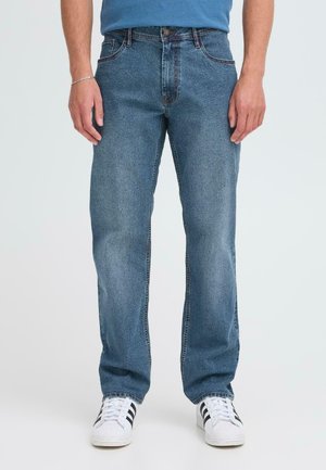 Blauwe denim spijkerbroeken met een relaxte pasvorm, riemlussen, voor- en achterzakken, en subtiele vervaging; gecombineerd met witte sneakers met zwarte strepen.