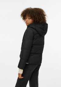 Sort puffjakke med hette, med vattert design, elastiske mansjetter og en tilpasset silhuett. Stoffet fremstår som glatt og matt.