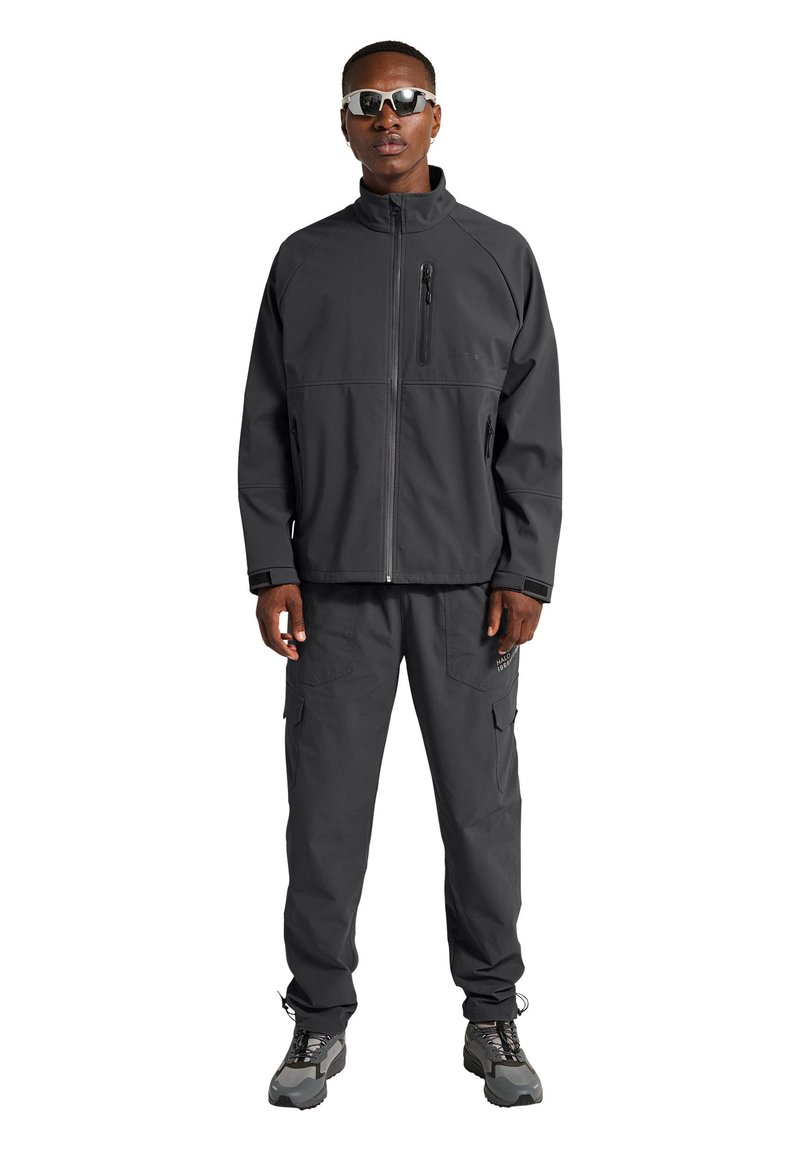 Czarna kurtka softshell z wysokim kołnierzem i zapinaną na zamek kieszenią na piersi, zestawiona z dopasowanymi spodniami cargo z bocznymi kieszeniami i subtelnym logo.