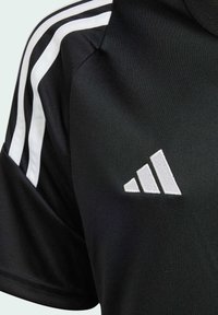 Svart atletisk skjorta med vit tre-stripes design på axeln och vitt broderat märke med tre diagonala ränder. Tillverkad av ett glättat tyg.